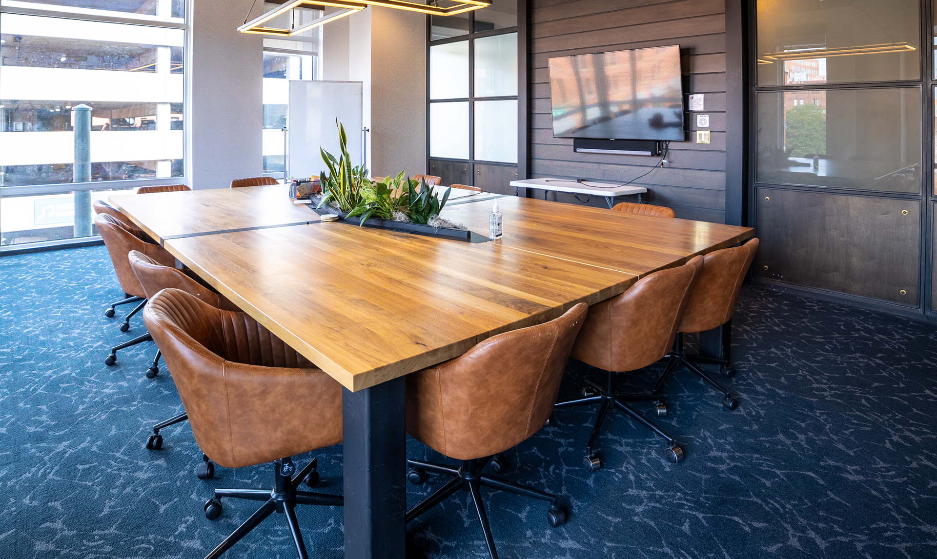 Modern coworking conference room with large wooden table, leather chairs, and tech amenities, ideal for team meetings and collaborative work at Vast Coworking.