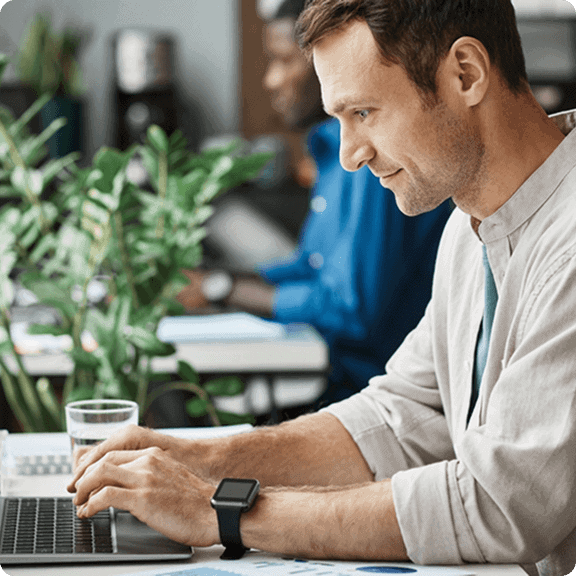 Man working on laptop at coworking space with greenery in background, modern office environment.