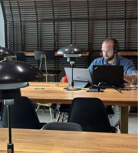 An individual working at a desk in Vast Coworking, equipped with a laptop, headphones, and modern lighting, showcasing a professional and collaborative environment aligned with "Our Framework.".