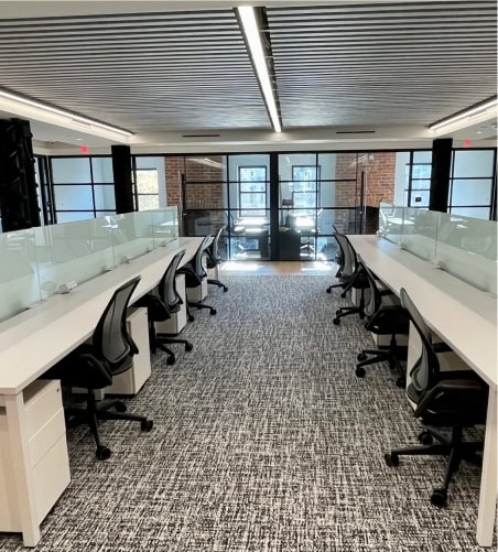 Coworking office with ergonomic chairs, white desks, and glass partitions in a bright, contemporary workspace.