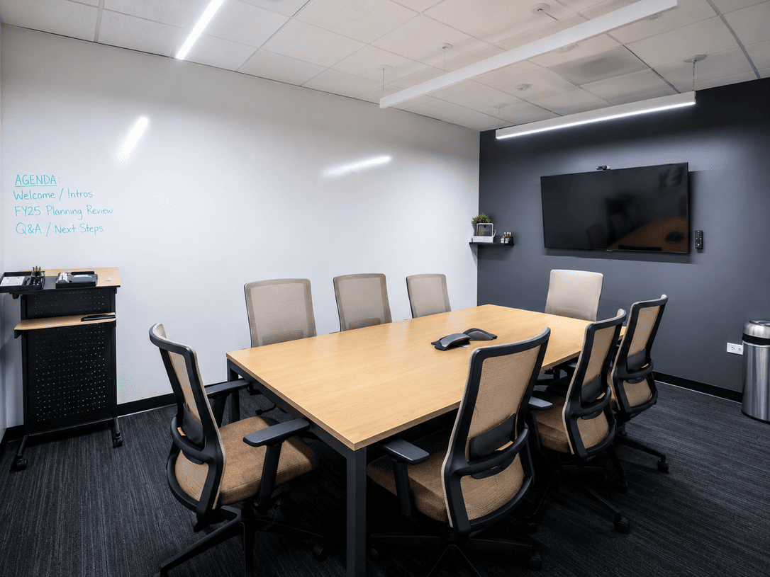 Modern coworking meeting room with a large wooden table and eight beige chairs, ideal for collaborative work at Vast Coworking.