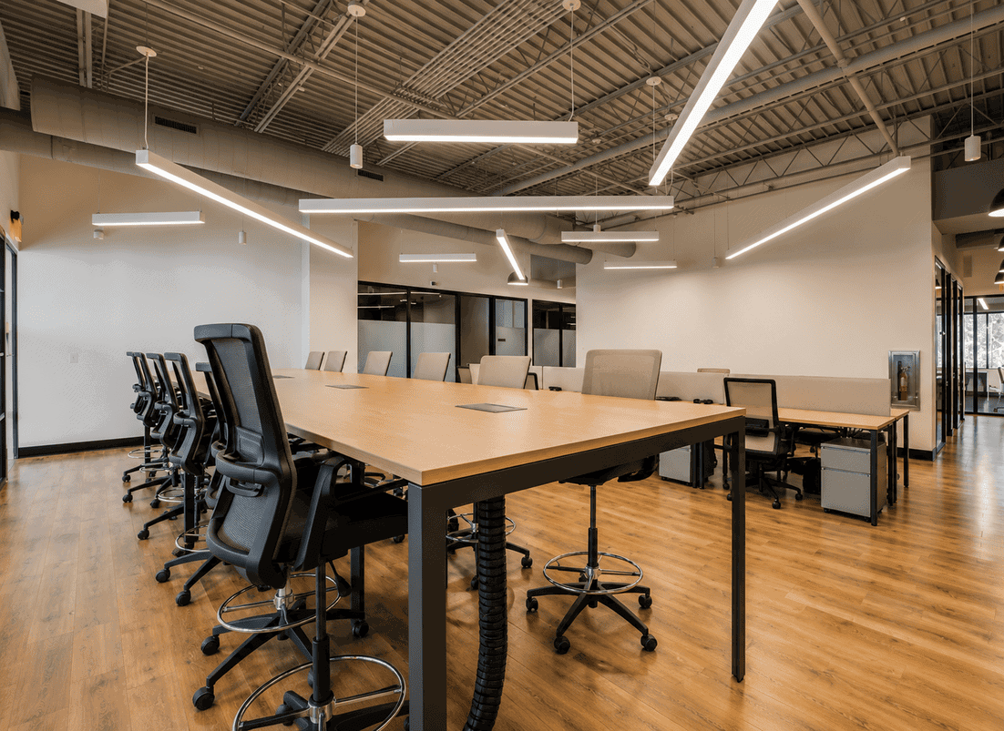 Modern coworking space with a large conference table, ergonomic chairs, and contemporary lighting fixtures.