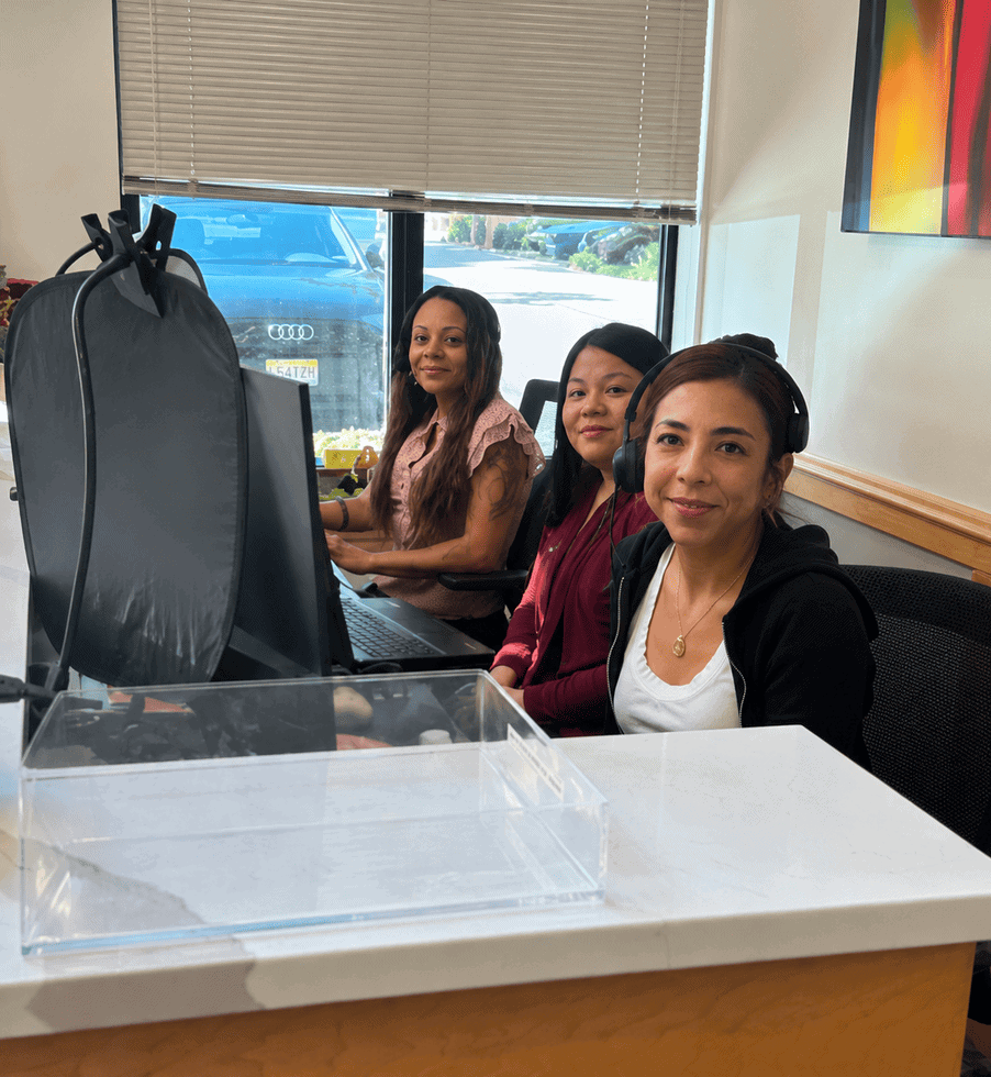 Three women working together at a coworking space with computers and a large window in the background.