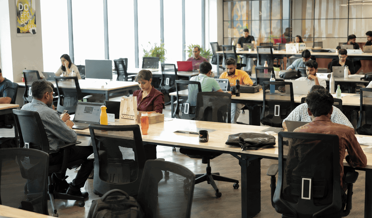 Modern coworking space with diverse professionals working at desks, large windows, and natural light, ideal for networking and productivity.