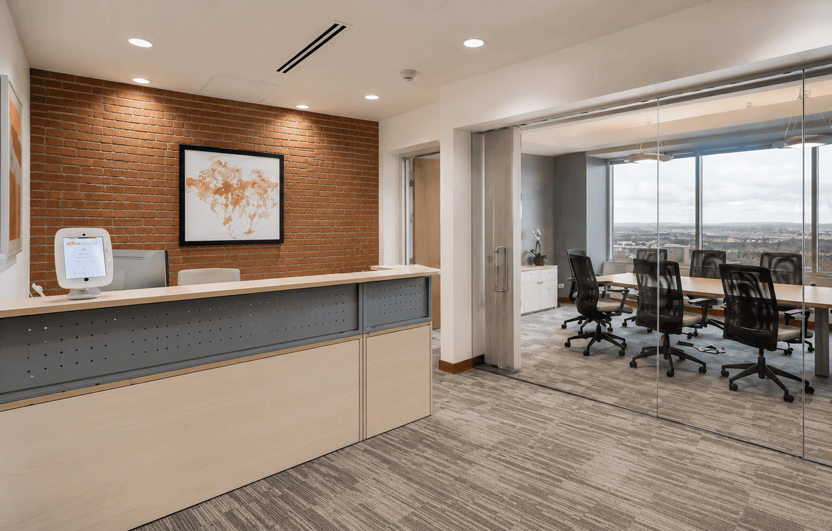 Modern coworking space reception area with a world map on the brick wall and a glass-walled conference room with city views.