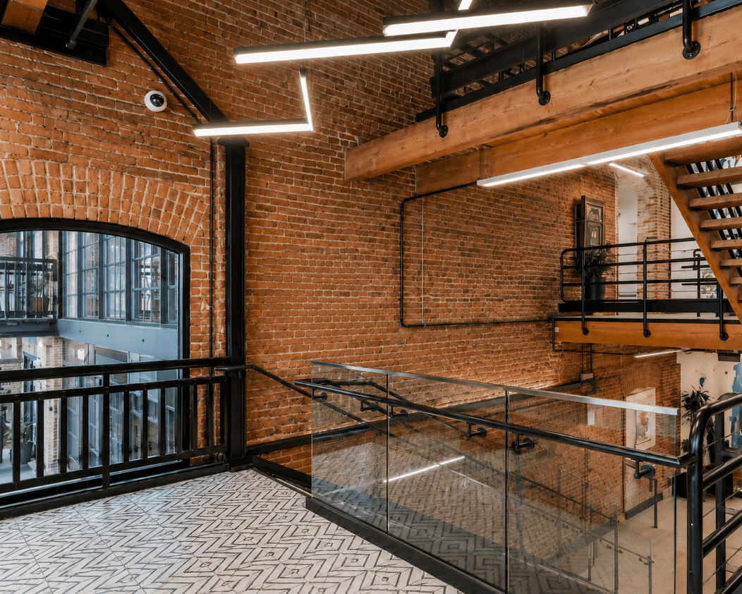 Modern coworking space with exposed brick walls, glass railings, and contemporary lighting fixtures.