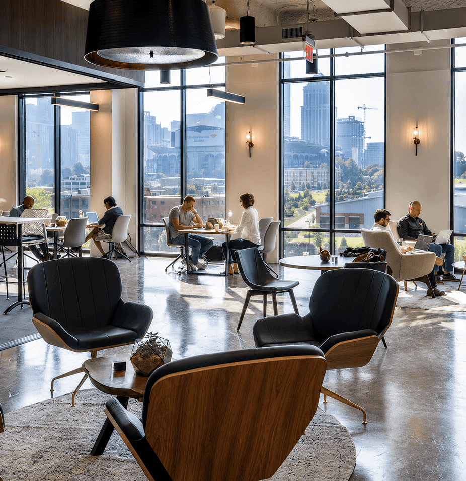 Modern coworking space with large windows, stylish seating, and people working in a bright, open environment.