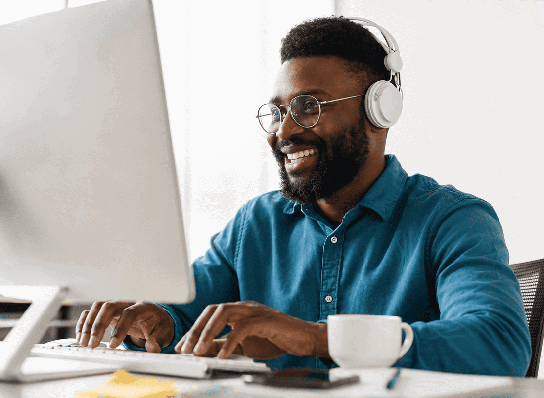 Smiling man with headphones working at a computer in a modern office setting.