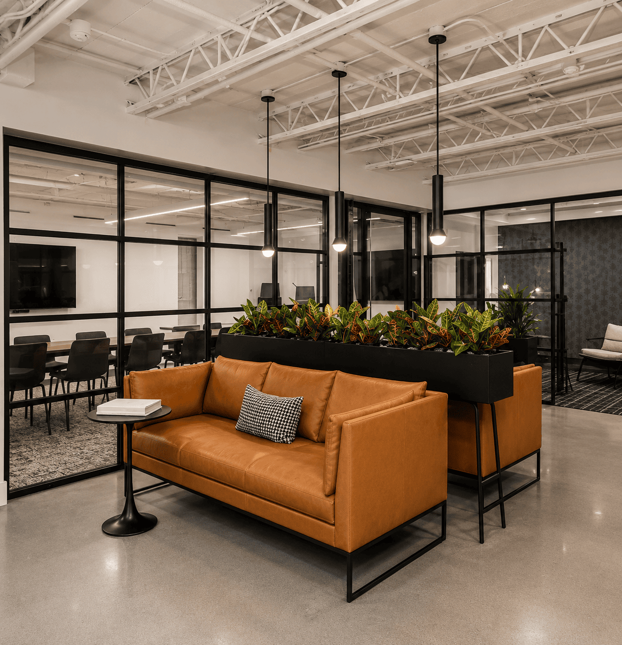 Modern coworking space with a tan leather sofa, black side table, and indoor plants in a bright, open office environment.